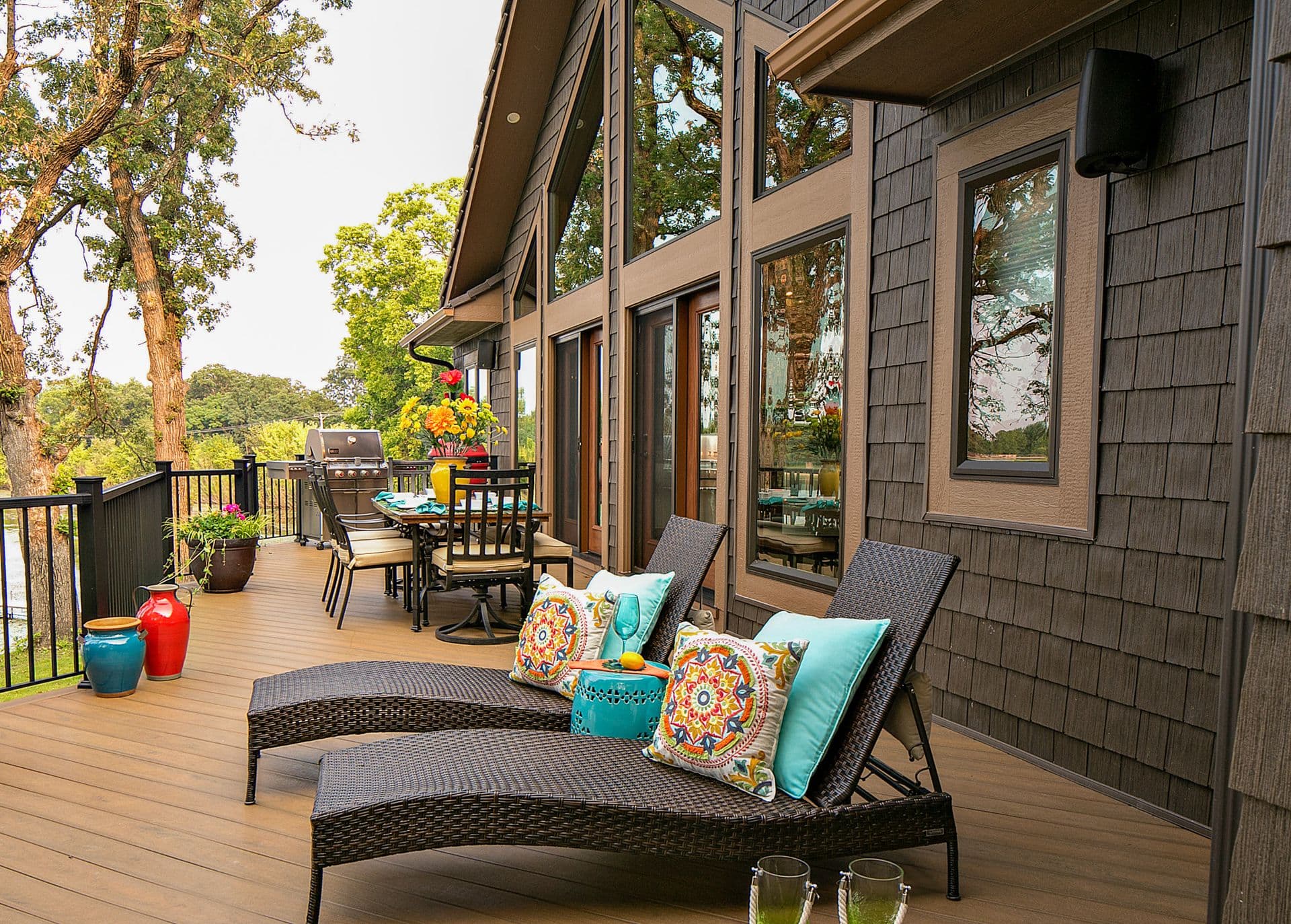 Spacious deck with lounge chairs, dining table, and grill overlooking wooded landscape, attached to modern home with large windows and cedar siding