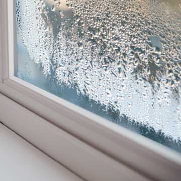 Condensation and frost coating a window pane, indicating moisture buildup and cold temperature against the glass