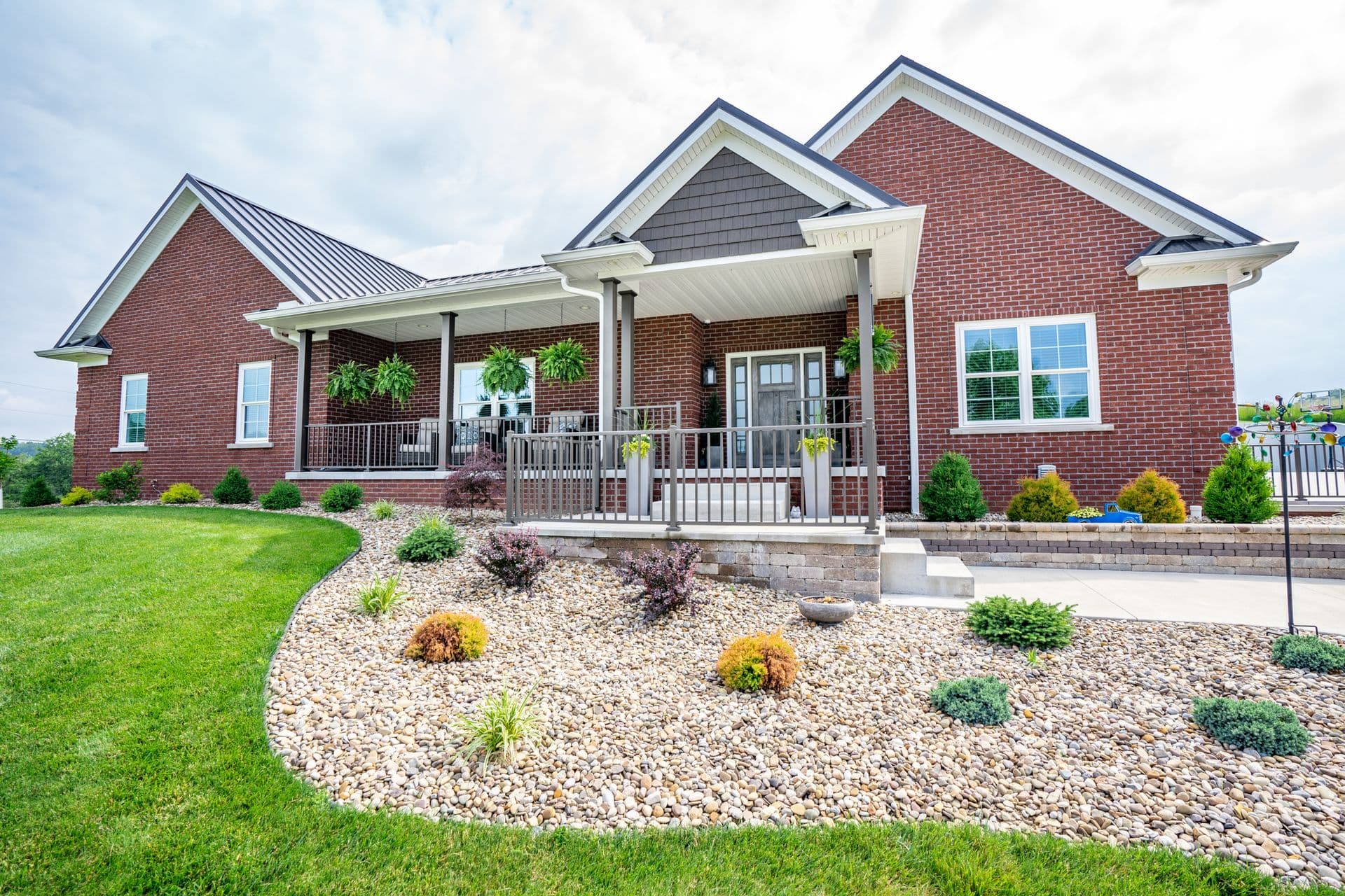 Red brick home with covered front porch, metal roof, white trim, and landscaped front yard with shrubs and gravel beds