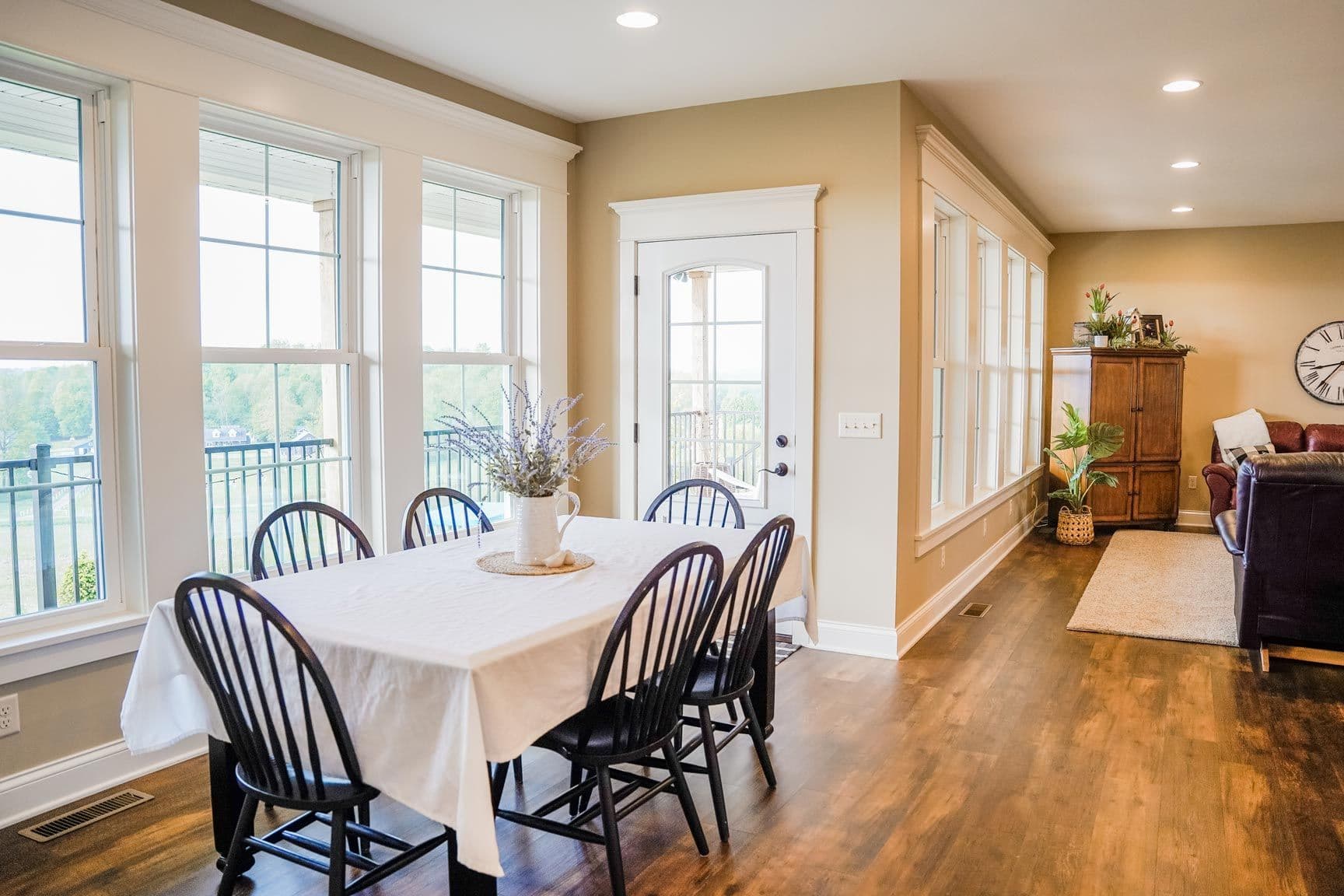 Bright dining room with round table, four black Windsor chairs, and large windows overlooking a deck and forested landscape