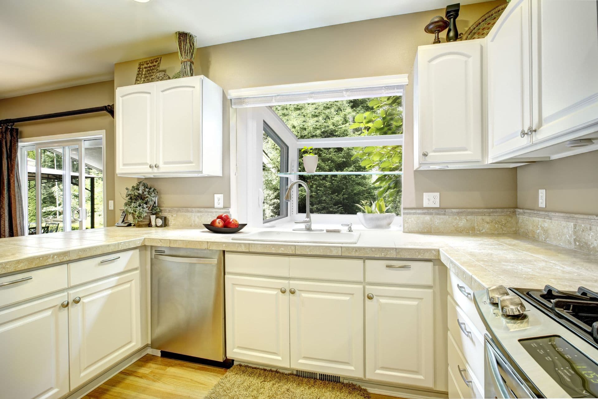 Bright kitchen with cream-colored cabinetry, granite countertops, stainless steel appliances, and large window overlooking green foliage