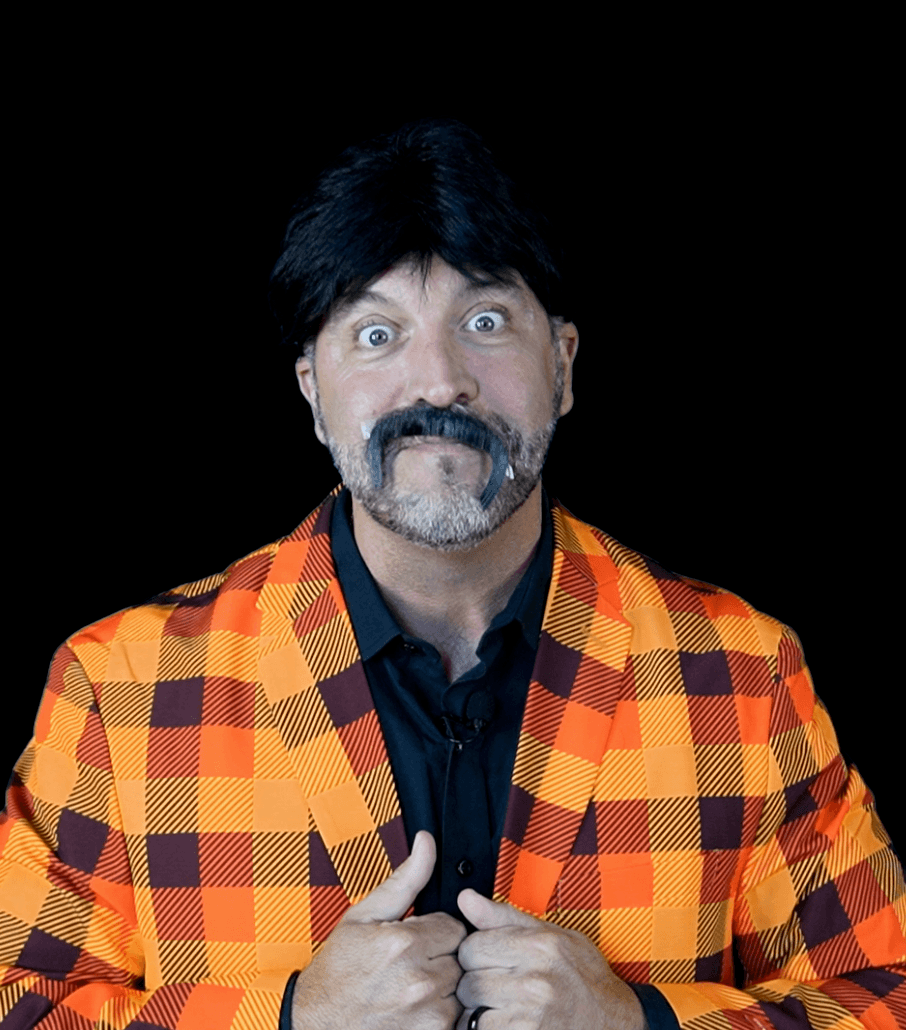 Man with dark hair and beard wearing orange and burgundy plaid jacket over black shirt, looking at camera with surprised expression against black background