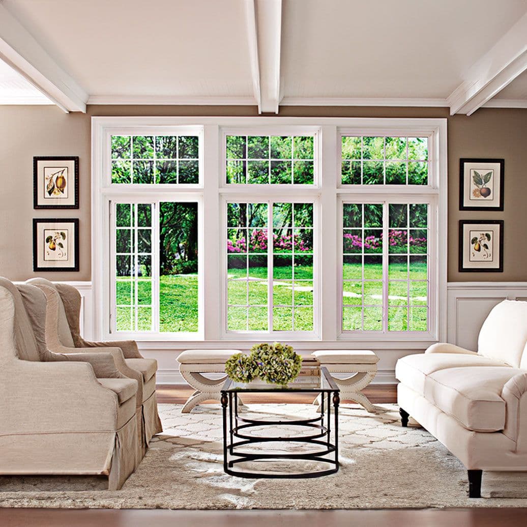 Elegant living room with large multi-pane windows overlooking gardens, neutral furnishings, botanical artwork on walls, and round coffee table with fresh floral arrangement