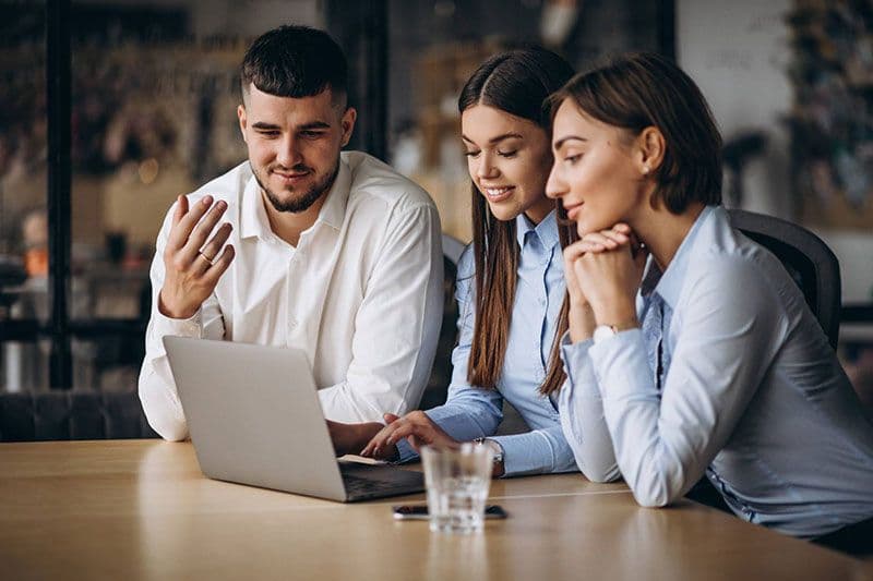 Three business professionals collaborating at a laptop during a work meeting, reviewing content on screen together