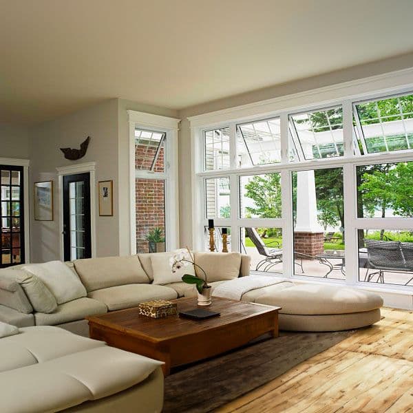 Bright living room with cream sectional sofa, wooden coffee table, and large multi-pane windows overlooking a brick patio and garden