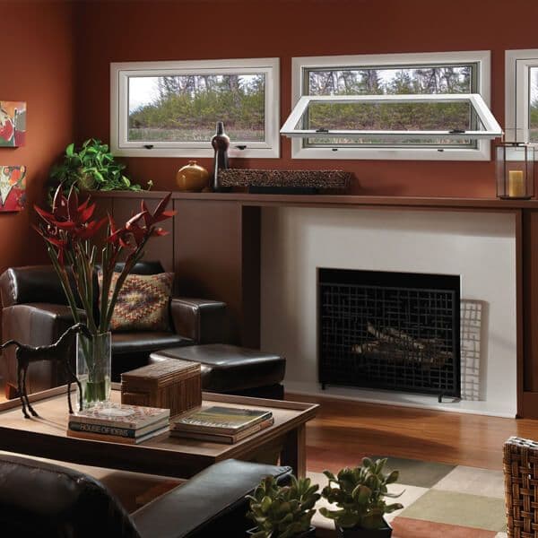 Warm living room with rust-colored walls, fireplace with black tile surround, wood shelving with windows above, leather seating, and fresh red flowers in glass vase on coffee table